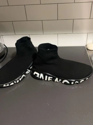 Balenciaga Speed Trainer svarta sneakers - Svarta Balenciaga Speed Trainer sneakers med stickad strumpdesign och tjock sula. Sulan är svart med vit Balenciaga-logga runtom. Skorna har en minimalistisk look och är tillverkade i textil och gummi.