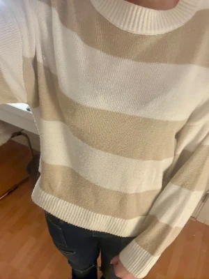 Randig beige och vit stickad tröja H&M - Mysig stickad tröja från H&M Divided i storlek S. Tröjan har breda beige och vita ränder, rund halsringning och ribbade muddar vid ärmslut och nederkant. Perfekt för lager på lager och chill vardagsstil.