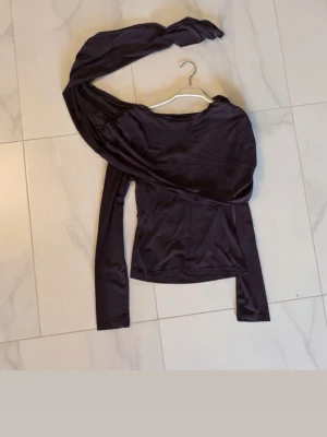 Brun oneshoulder meshblus - Trendig blus meshblus med oneshoulder-design och lång ärm. Tunt, stretchigt material som ger en cool och unik look. Perfekt för dig som vill sticka ut med en asymmetrisk stil och snygga detaljer.