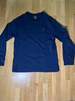 Mörkblå långärmad tröja Polo Ralph Lauren - Mörkblå långärmad tröja från Polo Ralph Lauren i mjuk bomull. Klassisk rund halsringning och ikonisk röd broderad logga på bröstet. 
