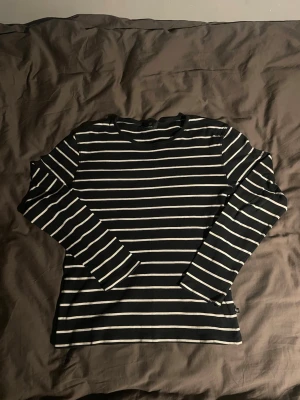 Mörkblå o vit randig långärmad topp - En mörkblå långärmad topp med vita horisontella ränder. Klassisk rak passform och rund halsringning. Perfekt att styla med jeans eller kjol för en enkel och stilren look.