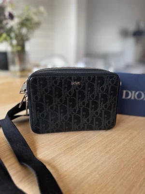 Dior Messenger Pouch  - MESSENGER POUCH BLACK DIOR OBLIQUE GALAXY LEATHER.   Snygg svart axelväska från Dior med ikoniskt monogrammönster över hela väskan. Väskan har en justerbar axelrem i tyg och silverfärgade detaljer. Perfekt storlek för det viktigaste och stängs med dragkedja. Klassisk och trendig design. Autenticitet kort och kvitton finns. Nypris 1400€. 