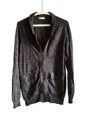 Mörkgrå ziptröja med fickor - Snygg mörkgrå ziptröja med två framfickor och ribbade muddar. Tröjan har en enkel krage och är tillverkad i ett mjukt, stickat material. Perfekt att slänga på sig över en t-shirt för en avslappnad look.