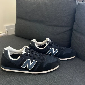 Svarta New Balance sneakers 373 (nypris 1099kr) - Snygga svarta New Balance sneakers med klassisk vit N-logga på sidan. Skorna har rund tå, platt sula och snörning. Ovandelen är i mesh och mocka för både stil och komfort. Perfekta för dig som gillar sportig och clean look.