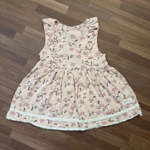 Blommig rosa klänning - Klänning från Newbie med rosa blommigt mönster, storlek 68 (4-6mån). Sparsamt använd utan anmärkningar. Söta volangdetaljer vid axlarna och spetskant längst ner.
