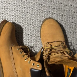 Beiga boots i mocka med snörning - Säljer ett par klassiska beiga boots i mocka med grov sula och snörning. Skorna har rund tå, guldfärgade öljetter och bruna detaljer vid ankeln. Perfekta för höst och vinter, riktigt snygga till jeans eller cargo pants.