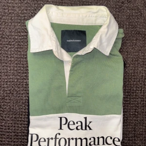 Peak Performance Rugger i nyskick - Peak Performance rugbytröja i storlek L. Fantastisk kvalitet och i perfekt skick. Tröjan har lång ärm och vit krage.. Stor Peak Performance-logga framtill. Tillverkad i bomull, perfekt för en sportig och avslappnad look.