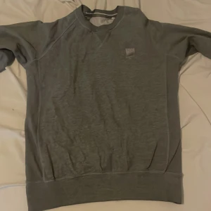 Grå sweatshirt med broderad logga MFF - En stilren grå sweatshirt från Peak Performance med broderad logga på bröstet. Tröjan har rund halsringning, långa ärmar och breda muddar vid ärmslut och nederkant. Perfekt för en chill och avslappnad look.