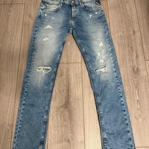Replay ljusblå slitna jeans herr - Säljer ett par ljusblå jeans från Replay med slitna detaljer och trasiga partier framtill. Klassisk femficksmodell med raka ben och normal passform. Jeansen är tillverkade i bomull och har en snygg tvättad look.