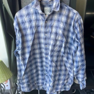 Blårutig skjorta från Terry Parker - Säljer en blårutig skjorta från Terry Parker i bomull. Skjortan har klassisk krage, knäppning framtill och en bröstficka. Mönstret är rutigt i blått och vitt, och modellen har långa ärmar. Perfekt för en avslappnad och cool stil.