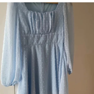 Ljusblå långklänning med puffärm - Superfin ljusblå långklänning med diskret prickigt mönster och puffiga långärmar. Klänningen har rynkade detaljer vid bysten och en luftig känsla, perfekt för vår och sommar. Söt och romantisk stil som verkligen sticker ut.