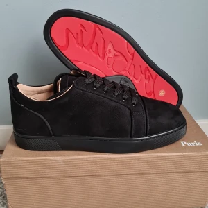 Christian Louboutin svarta sneakers mocka - Snygga svarta sneakers från Christian Louboutin i lyxig mocka med ikonisk röd sula. Skorna har rund tå, platt sula och svarta snören. Insidan är ljusbeige och designen är clean men ändå exklusiv med diskret broderad logga på hälen.