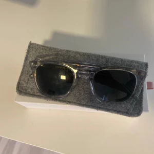 Grå transparenta solglasögon SmartEyes - Snygga solglasögon från SmartEyes med transparent grå båge och mörka glas. Klassisk, lite fyrkantig form som passar till många stilar. Kommer med ett grått fodral i filtmaterial. Perfekta för soliga dagar!