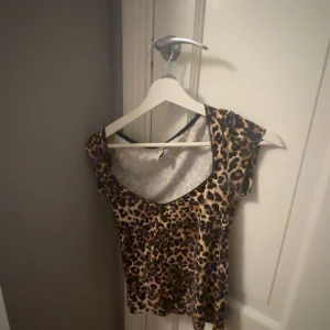 Leopardmönstrad topp med rund hals - ALDRIG ANDVÖND. Säljer en snygg leopardmönstrad topp med rundad hals och korta ärmar. Toppen har svarta spetsdetaljer längs halsringningen och är i mjukt, stretchigt material. 