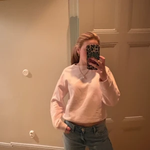 Ljusrosa sweatshirt i bomull - Enkel och snygg ljusrosa sweatshirt med rund hals och långa ärmar. Tröjan har en croppad passform och breda muddar vid ärmslut och midja. Perfekt för dig som gillar en clean och chill stil.