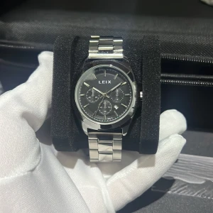 LEIX silverfärgad klocka med svart urtavla - Stilren klocka från LEIX med svart urtavla och flera små urverk. Armbandet är i blankt och borstat silverfärgat stål med viklås. Klockan har tydliga indexmarkeringar och datumvisning, perfekt för dig som gillar en klassisk och modern look.