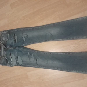 Lågmidjade slitna blå jeans från Onlyjeans - Säljer ett par blå jeans från Onlyjeans med låg midja och bootcut-ben. Jeansen har flera stora slitningar och hål framtill för en riktigt edgy look. Klassisk femficksmodell med dragkedja och knapp. Perfekta för dig som gillar streetstyle. Midjemått:35    Innerbenslängd: 76. Skriv om ni har några fler frågor!