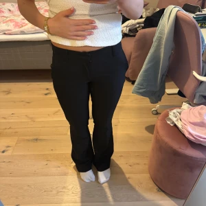 Svarta bootcut kostymbyxor - SÄLJER 2 PAR EXAKT LIKADANA!!!Snygga svarta kostymbyxor med bootcut-snitt och klassisk midja. Byxorna har en stilren look med fickor bak och fram, samt stängs med dragkedja och knapp. Perfekta för dig som gillar en clean och tidlös stil. 