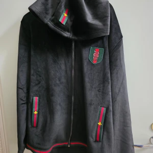 GG tracksuit  - Svarta mjukisbyxor i mjukt sammetstyg med snörning i midjan. Snygga röd-gröna band med broderad gul detalj vid fickorna och benslut. Byxorna har en loose passform och ribbade muddar. Perfekta för chill dagar och streetwear-vibe. Priset kan diskutera!!!!