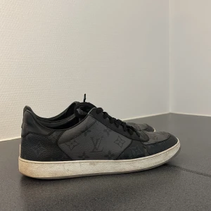 Svarta Louis Vuitton sneakers - Svarta sneakers från Louis Vuitton med klassiskt monogrammönster över hela skon. Skorna har snörning, rund tå och platt vit sula. Tillverkade i skinn med detaljer i mörkgrått och svart, samt Louis Vuitton-logga på hälen och ovansidan. Lite små skador här o där men annars fina. Kvitto box och allt finns med