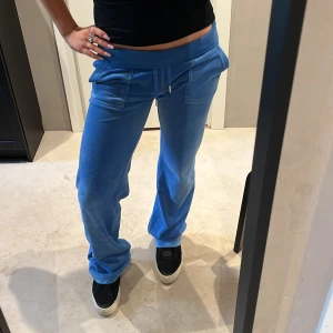 Snygga Juicy Couture - Snygga blå mjukisbyxor i mjukt velourmaterial med bred midja och snörning framtill. Byxorna har raka ben, stora fickor och en avslappnad passform som ger en chill vibe. Perfekta för att hänga hemma eller dra till stan med kompisarna. Skriv innan köp!!❤️
