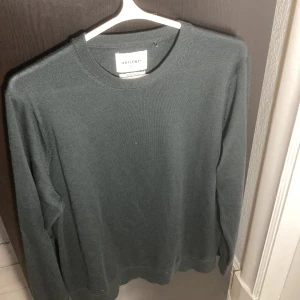 Mörkgrå merinoullströja från Vailent - Säljer en stilren mörkgrön tröja från Vailent i mjuk merinoull. Tröjan har rund halsringning, lång ärm och en clean look utan mönster eller detaljer. Perfekt för dig som gillar enkel och klassisk stil. Tröjan ser lite grå ut på bilderna men är mer åt de mörkgröna hållet egentligen. Passar runt 185-190