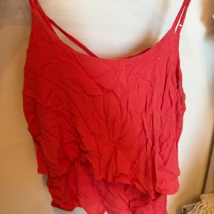 Röd linnetopp med justerbara band - Säljer en röd linnetopp från Bik Bok med tunna, justerbara axelband. Toppen har en luftig och skrynklig struktur som ger en cool vibe. Perfekt för varma dagar och enkel att styla med jeans eller kjol. Färgen är intensivt röd och materialet känns lätt mot huden.