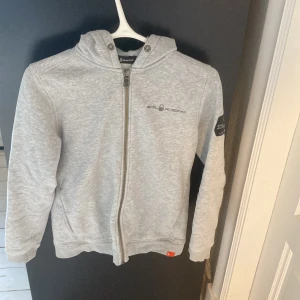 Grå hoodie från Sail Racing  - Snygg sail racing full zip med snyggt tryck på ryggen, köpt på Marstrand för 1500, säljer för 450. Passar runt 170-175. Kom med bud!