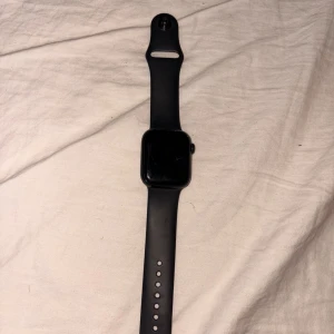 Svart Apple Watch med silikonarmband - Snygg svart Apple Watch med fyrkantig urtavla och mjukt silikonarmband. Klockan har en modern och stilren design med digital krona på sidan. Perfekt för dig som gillar teknik och vill ha koll på notiser och hälsa direkt på handleden.