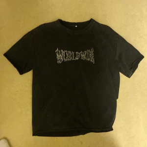 Svart t-shirt med Worldwide-tryck - Svart t-shirt med coolt 'WORLDWIDE'-tryck på bröstet i vit text. Klassisk passform med rund hals och korta ärmar. Perfekt för dig som gillar streetwear och vill ha en enkel men snygg look. Passar perfekt på gymmet