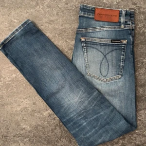 Calvin Klein Slim Taper jeans blå W29 L32 - Snygga blå jeans från Calvin Klein Jeans i modellen Slim Taper. Jeansen har klassisk femficksdesign, ljus tvätt med slitningar och logga på bakfickan samt läderpatch i midjan. Perfekt passform med smalare ben och normal midja.