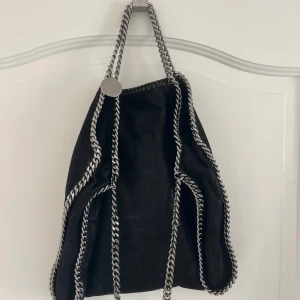 Svart axelväska Stella McCartney - Säljer en svart Stella McCartney large falabella Tote bag!  Väskan är köpt via affordable luxury så kvitto och äkthetsbevis finns. Väska köptes 2020 men knappt använd, max 10 gånger. 