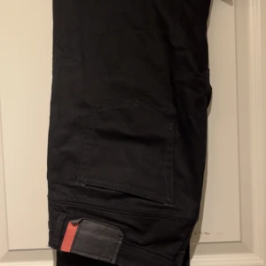 Acne Studios 36/34 straight leg ish - Svarta jeans från Acne Studios Blå Konst med klassisk femficksdesign och snygg detalj i form av svart och rött läderpatch bak i midjan. Jeansen har raka ben och är tillverkade i kraftig bomullsdenim. Perfekta för dig som gillar stilrena och moderna byxor.