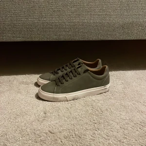 Olivgröna sneakers från Zara - Snygga olivgröna sneakers från Zara med stilren design. Skorna har en matt finish, matchande snörning och vit platt sula. Insidan är beige och materialet känns som syntet med en mjuk känsla. Perfekta för dig som gillar minimalistisk och clean stil.
