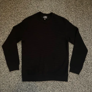 Svart ribbad tröja från H&M - Svart långärmad tröja från H&M i regular fit. Tröjan har ett ribbat tyg som ger en snygg struktur och är tillverkad i mjuk bomullsmix. Perfekt basic med rund halsringning och muddar vid ärmslut och nederkant. Knappt använt 