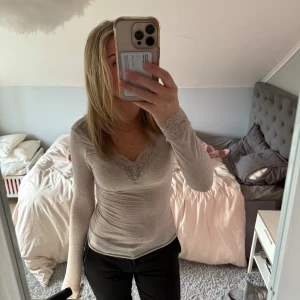Intimissimi topp med spetsdetaljer  - Beige långärmad topp från intimissimi med v-ringning och spetsdetaljer både vid halsringningen och vid ärmsluten. Toppens material är mjukt och stretchigt. Använt väldigt fåtal gånger så den är i ett väldigt fint skick.