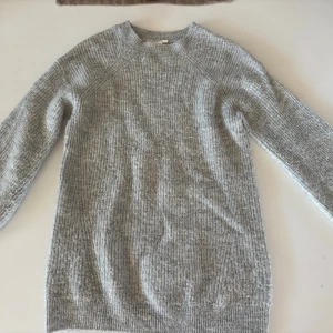 Ljusgrå stickad tröja med ribbad struktur - Mysig ljusgrå stickad tröja med ribbad struktur och rund hals. Tröjan har långärmade ärmar och är tillverkad i ett mjukt material som passar perfekt när det är kallt ute. Enkel och stilren design som är lätt att matcha med andra plagg.