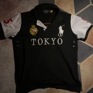 Polo Ralph Lauren Chief keef Tokyo - Snygg svart pikétröja från Polo Ralph Lauren med vita ärmar, stora röda siffror på ärm och rygg, samt broderad Tokyo-text och emblem framtill. Klassisk polokrage och slim fit. Storleken är L men den passar M 