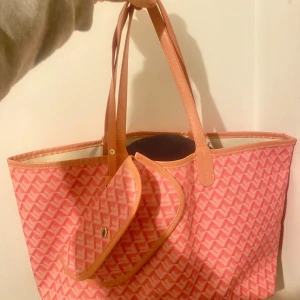 Rosa shoppingväska med mönster - Stor rosa shoppingväska med ljusrosa och vita zigzag-mönster, matchande handtag och en liten avtagbar ficka framtill. Väskan har en öppen topp och är perfekt för att bära allt du behöver. Materialet är troligtvis syntet med detaljer i faux-skinn.