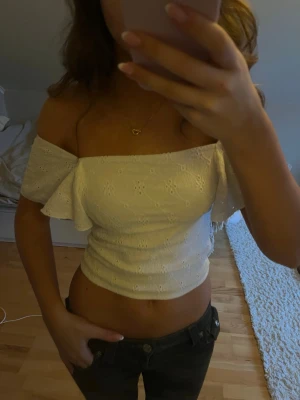 Vit croppad offshoulder blus - Säljer en söt vit blus med broderade detaljer och offshoulder-modell. Toppen är croppad och har korta, volangiga ärmar. Perfekt för sommarens varma dagar och ger en romantisk vibe till outfiten. Toppen är ifrån Kappahl. 