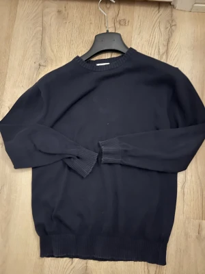 Mörkblå stickad tröja från Kappahl - Snygg mörkblå stickad tröja från Kappahl i storlek 146/152. Tröjan har rund hals, ribbade muddar vid ärmslut och nederkant samt långärmad passform. Perfekt för dig som gillar enkel och klassisk stil.