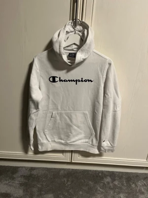 Vit Champion hoodie  - Säljer en vit Champion hoodie med mörkblå text perfekt till vardag och fungerar även till sköna mysdagar. Det är storlek 162/167 Säljs för 249kr.