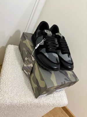 Valentino Rockrunner sneakers camo svart - Säljer ett par Valentino Rockrunner sneakers i svart och grått med camouflagemönster. Skorna har snörning, mesh och mockadetaljer samt en chunky gummisula. Märkeslogga på plösen och coola detaljer som gör dem riktigt unika.