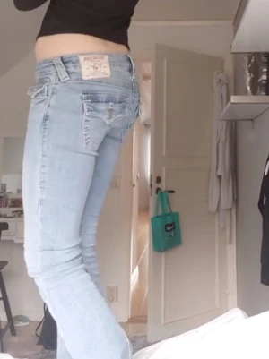 True Religion Joey Low Rise Flare jeans - Säljer ett par ljusblå True Religion Joey Low Rise Flare jeans i storlek 24 då de är förstora. De har snygga broderade fickor med silverknappar och klassisk label bak. Modellen är lågmidjad med bootcut och tillverkad i mjukt jeanstyg. Perfekt för dig som gillar detaljer och ikonisk stil. Byxorna ser lite fläckiga ut men det är min kamera som är trasig då man ser på första bilden att de INTE är fläckiga. Haft i ungefär ett halvår då de är bra skick.