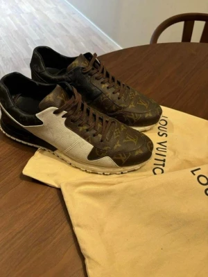 Louis Vuitton sneakers monogram brun/vit - Säljer ett par Louis Vuitton sneakers i klassiskt monogrammönster i brunt och guld, kombinerat med vita och svarta paneler. Skorna har bruna snören, rund tå och platt sula. Tillverkade i skinn med tydliga LV-detaljer och ikoniska loggor. Perfekta för dig som vill sticka ut med lyxig streetstyle.