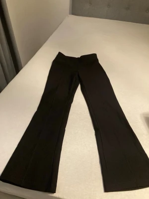 Svarta bootcut kostymbyxor - Snygga svarta kostymbyxor med bootcut-snitt och hög midja. Byxorna har en stilren design med raka ben som breddas nedtill och är gjorda i ett mjukt material som ger en skön passform. 