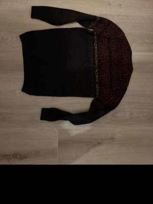 Svart och röd stickad tröja Defacto - Säljer en svart stickad tröja från Defacto i storlek XS med rött geometriskt mönster upptill. Tröjan har långärmade och ribbade muddar vid ärmslut och nederkant. Perfekt för dig som gillar grafiska detaljer och vill ha en mysig look.