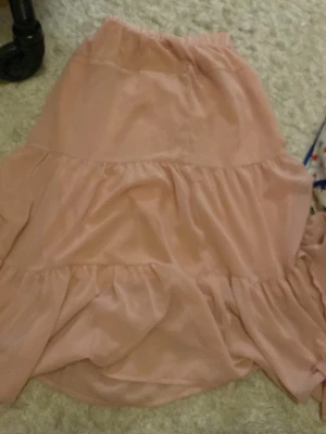 Ljusrosa volangkjol från DAZY - Supersöt ljusrosa långkjol från DAZY med bred resår i midjan och flera volanglager som ger en flowy och feminin look. Kjolen är gjord i ett mjukt och lätt material som känns skönt mot huden. Perfekt för dig som gillar romantiska vibes och vill sticka ut med en färgklick.