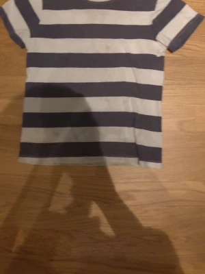 Randig t-shirt från Polarn O. Pyret - Säljer en klassisk t-shirt från Polarn O. Pyret med breda marinblå och vita ränder. T-shirten har korta ärmar och rund hals. Tillverkad i mjuk bomull som är skön att ha på sig hela dagen.