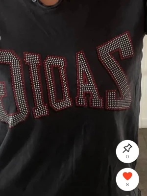 Svart t-shirt med paljetttext - Cool svart t-shirt med stor text framtill dekorerad med små paljetter och röda detaljer. T-shirten har rund hals och korta ärmar, perfekt för dig som gillar statement-plagg med lite bling.